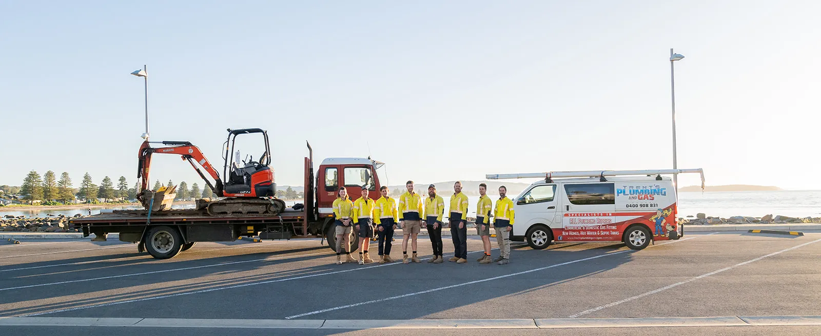 Panoramic team photo with branded vehicles, machinery and the coast behind